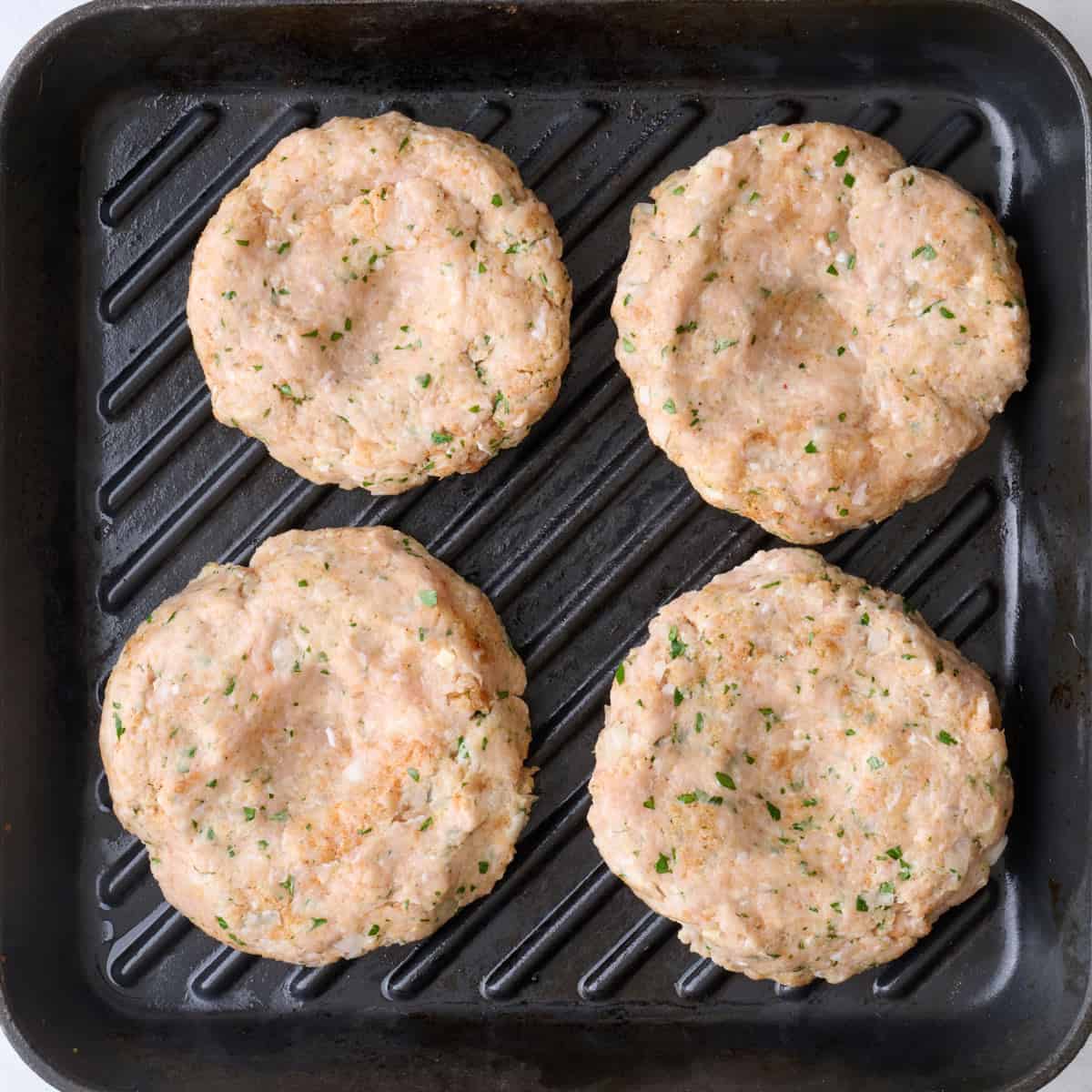 Chicken burger patties on a grill pan with indention in center of each one.