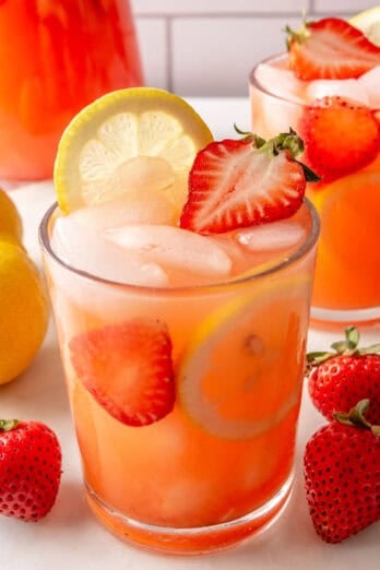 Two glasses of fresh strawberry lemonade filled with ice and ice fresh strawberries and lemon slices.