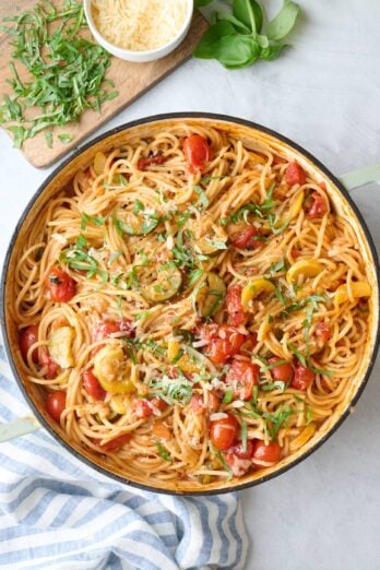 One pot veggie spaghetti garnished with parmesan and basil, small dish of extra cheese nearby.